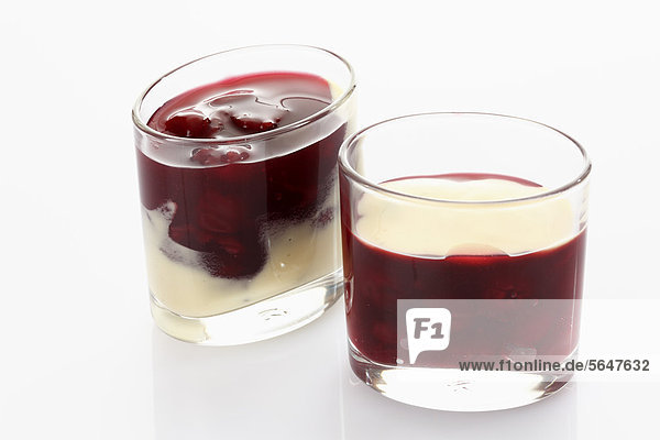 Glass with red fruit jelly and vanilla sauce on white background