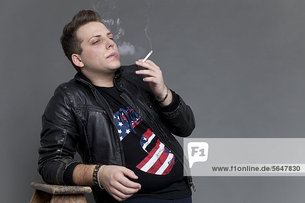 Junger Mann in Lederjacke raucht Zigarette und stützt sich lässig auf alte Holzleiter
