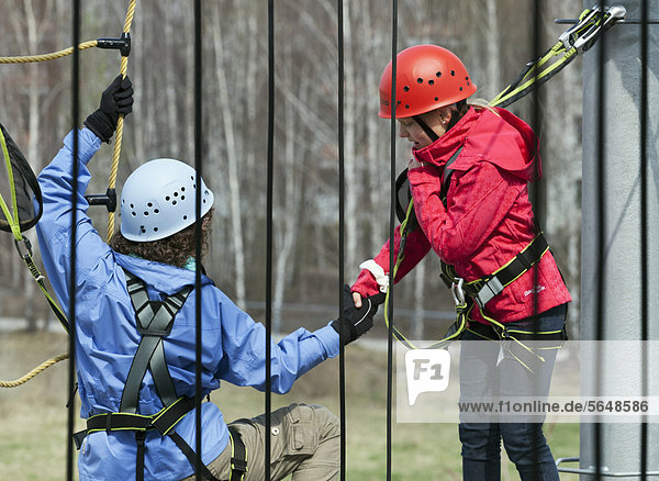 10-year-old girl reaching out to somebody climbing in a high rope course  Berlin  Germany  Europe