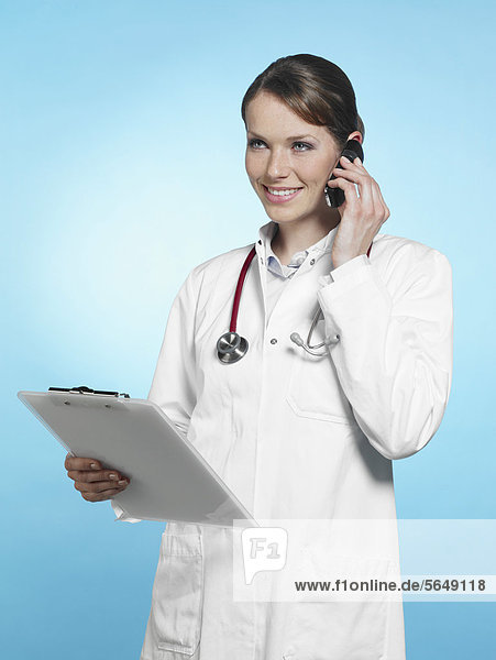 Ärztin auf dem Handy mit Stethoskop und Klemmbrett  lächelnd