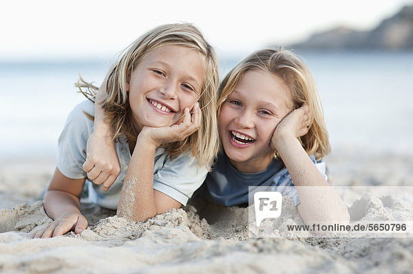 Spanien  Mallorca  Kinder im Sand am Strand liegend  lächelnd  Portrait
