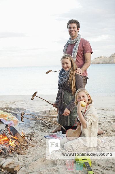 Spain  Mallorca  Friends with sausages at camp fire on beach