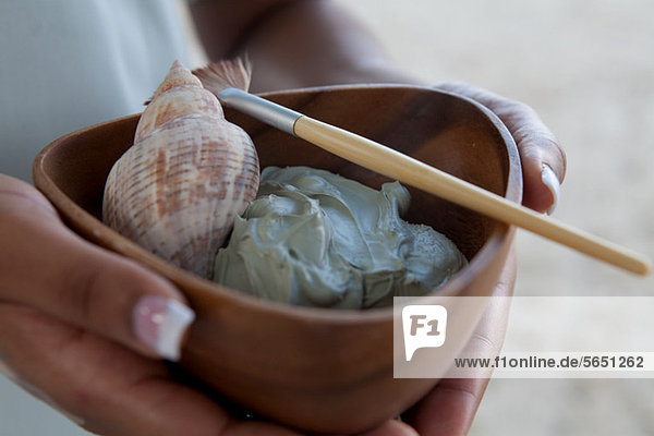 Person holding bowl of mud face mask and shell at spa