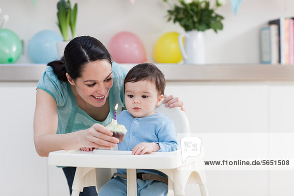Mother giving birthday cupcake to baby son in high chair