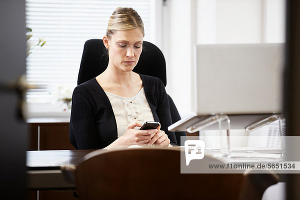 Geschäftsfrau am Schreibtisch  Blick aufs Handy