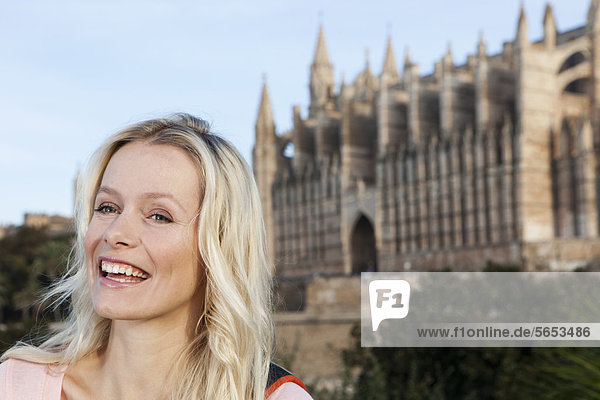 Spanien  Mallorca  Palma  Junge Frau stehend mit St. Maria Kathedrale im Hintergrund  lächelnd
