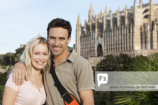 Spanien  Mallorca  Palma  Paar stehend mit St. Maria Kathedrale im Hintergrund  lächelnd  Portrait