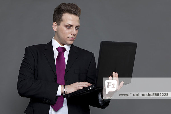 Junger Mann im Business-Look mit Anzug und Krawatte  mit Notebook