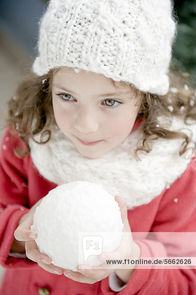 Mädchen mit Winterkleidung hält Schneeball