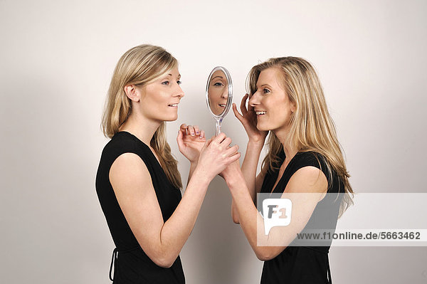 Twin sisters looking from both sides into a hand mirror