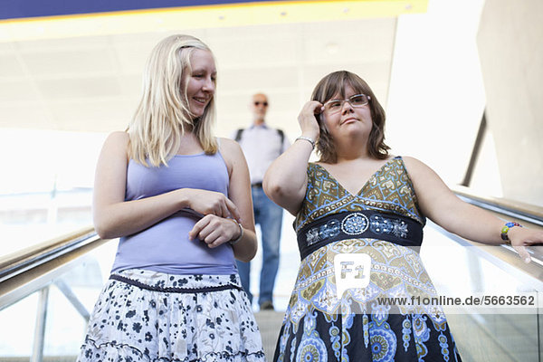 Lächelnde Frau mit Down-Syndrom und ihre persönliche Assistentin auf der Rolltreppe