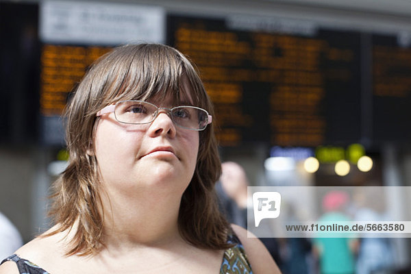 Junge Frau mit Down-Syndrom am Bahnhof mit Blick auf die Abfahrtstafel
