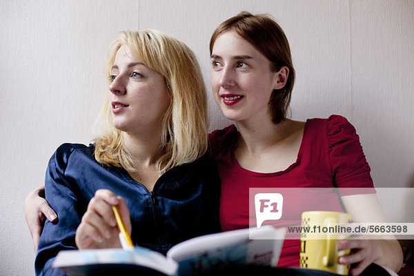 Two female friends with book and cup looking away over colored background