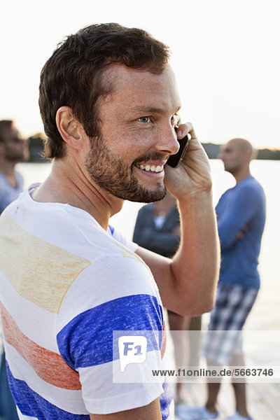 Smiling man speaking on call with friends in background