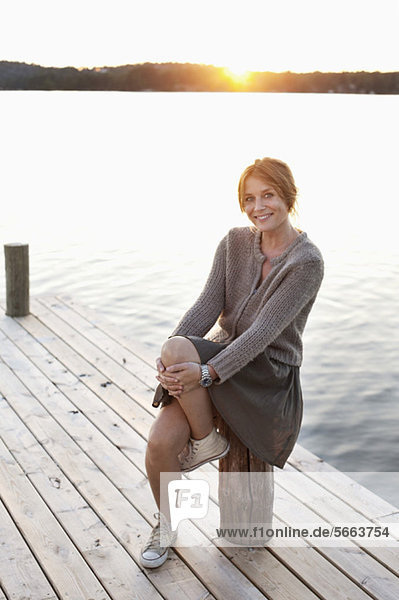 Ganzkörperporträt einer erwachsenen Frau  die auf dem Pier sitzt