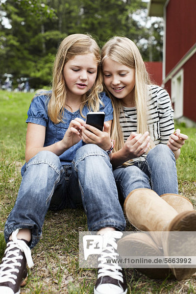 Sisters sitting in back yard looking at something in mobile phone