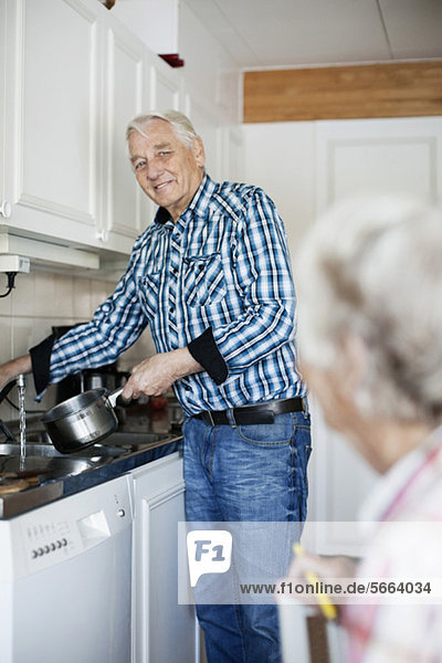 Älterer Mann beim Waschen von Utensilien  während er seine Frau ansieht.