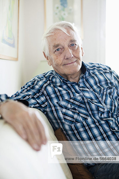 Porträt eines lächelnden älteren Mannes  der auf dem Sofa sitzt.