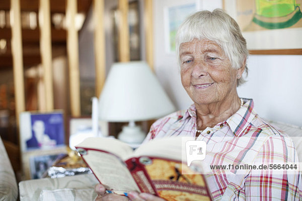 Glückliche Seniorin beim Lesen von Romanen im Liebeszimmer