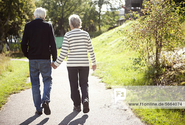 Rear view of active senior couple holding hands while walking in park