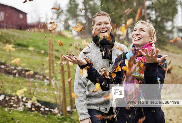 Paar genießt mit Herbstblättern  die auf sie fallen.