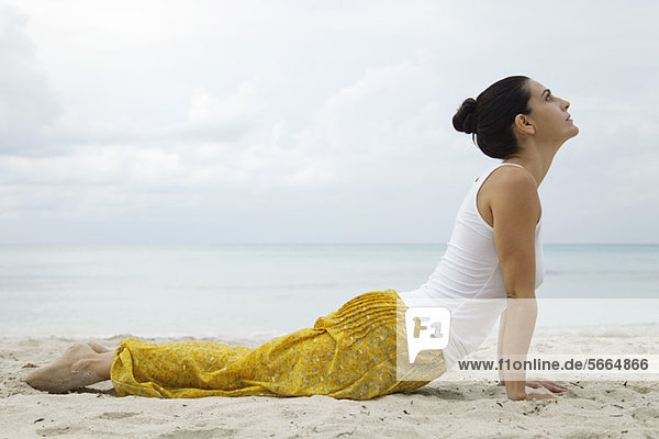 Mature woman in cobra pose on beach  side view