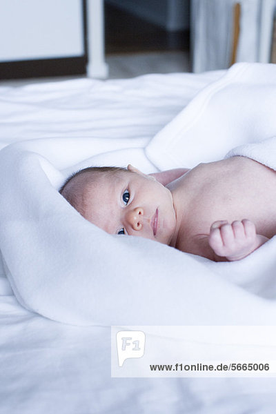 Neugeborenes Baby auf dem Bett liegend  mit Blick auf die Kamera