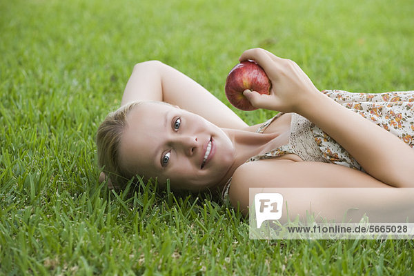 Junge Frau auf Gras liegend  Apfel haltend