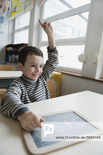 Junge am Schreibtisch sitzend mit Kreidetafel  handgehoben