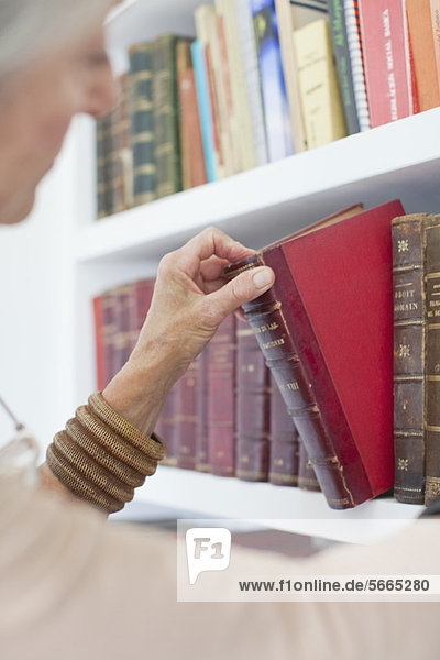Senior woman choosing book from bookshelf