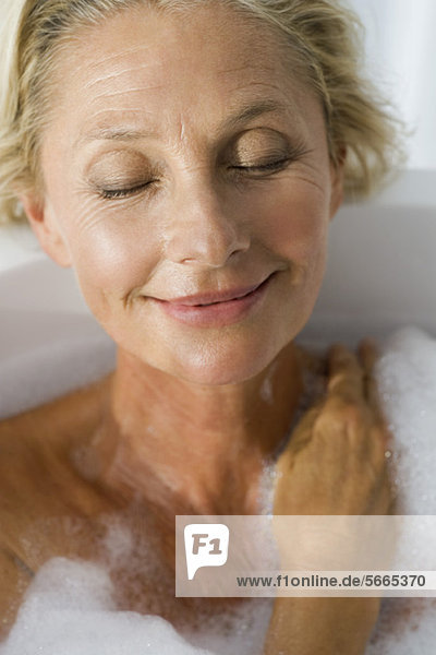 Mature woman relaxing in bubble bath with eyes closed  portrait