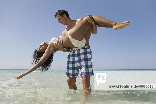 Paar zusammen am Strand  Mann trägt Frau im Wasser