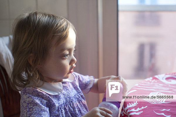 Kleinkind Mädchen hält Babyflasche  schaut in Gedanken weg