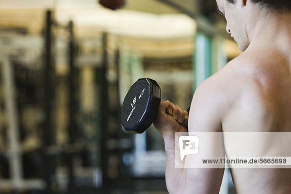 Barechested young man lifting dumbbell  rear view