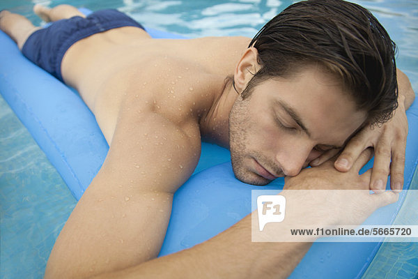 Junger Mann auf dem Bauch liegend auf einem aufblasbaren Schwimmer