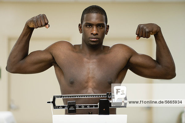 Young man flexing muscle on weight scale  portrait