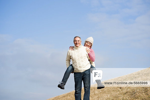Smiling man carrying woman piggyback in meadow