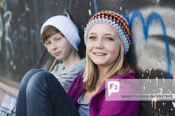 Teenagerin und Junge sitzen an einer Graffitiwand