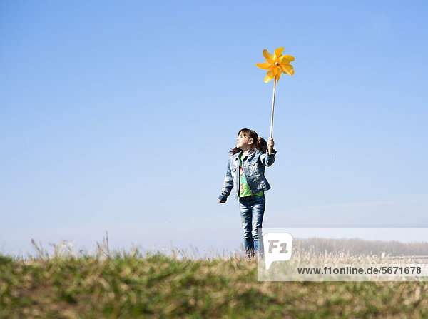 Mädchen steht mit Windrädchen auf einer Wiese