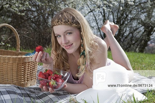 Blonde Frau liegt mit Erdbeeren auf einer Decke