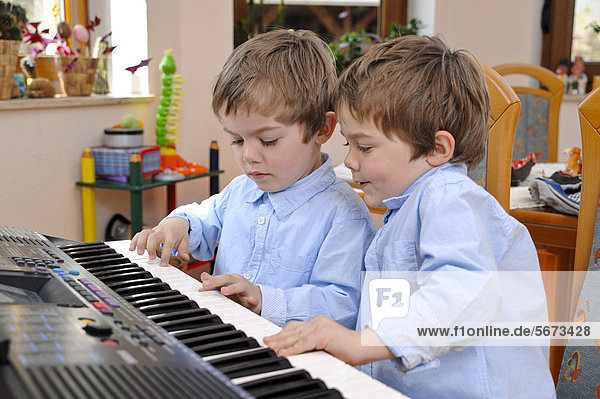 Zwillinge  Jungen  4 Jahre  machen gemeinsam Musik auf einem Keyboard