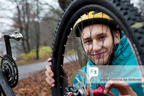 Junger Mann befestigt Fahrradrad im Wald