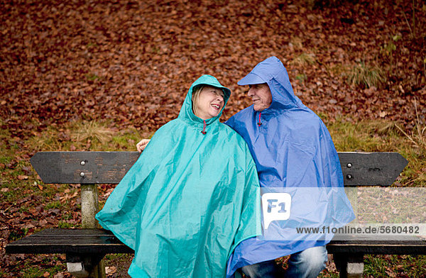 Senior couple sitting on park bench wearing waterproofs