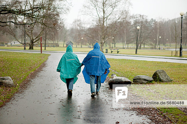 Senior couple in waterproof clothing walking through park