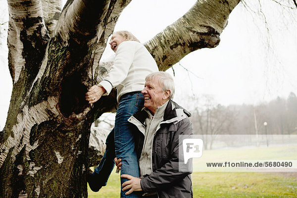 Senior man helping woman climb tree in park
