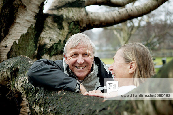 Senior couple leaning against tree  smiling