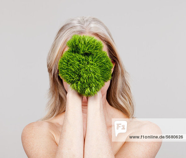 Reife Frau hält Pflanze vor dem Gesicht
