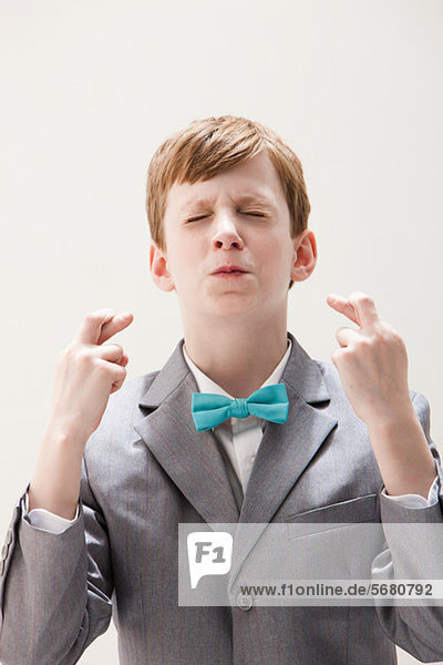 Boy wearing grey suit with fingers crossed  studio shot