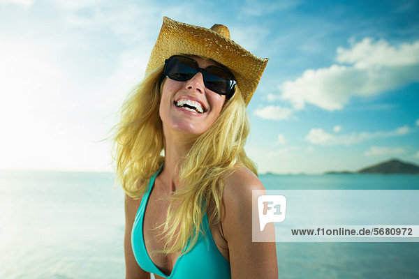 Glückliche Frau mit Sonnenbrille und Cowboyhut am Meer