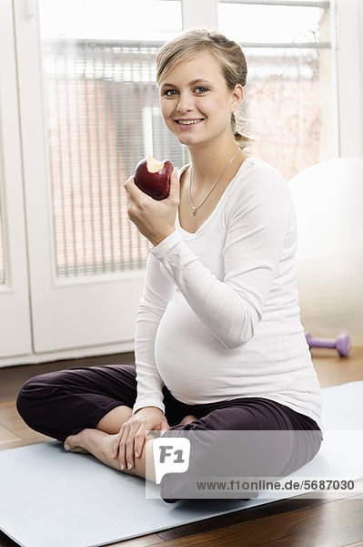 Schwangere Frau isst Apfel auf Yogamatte